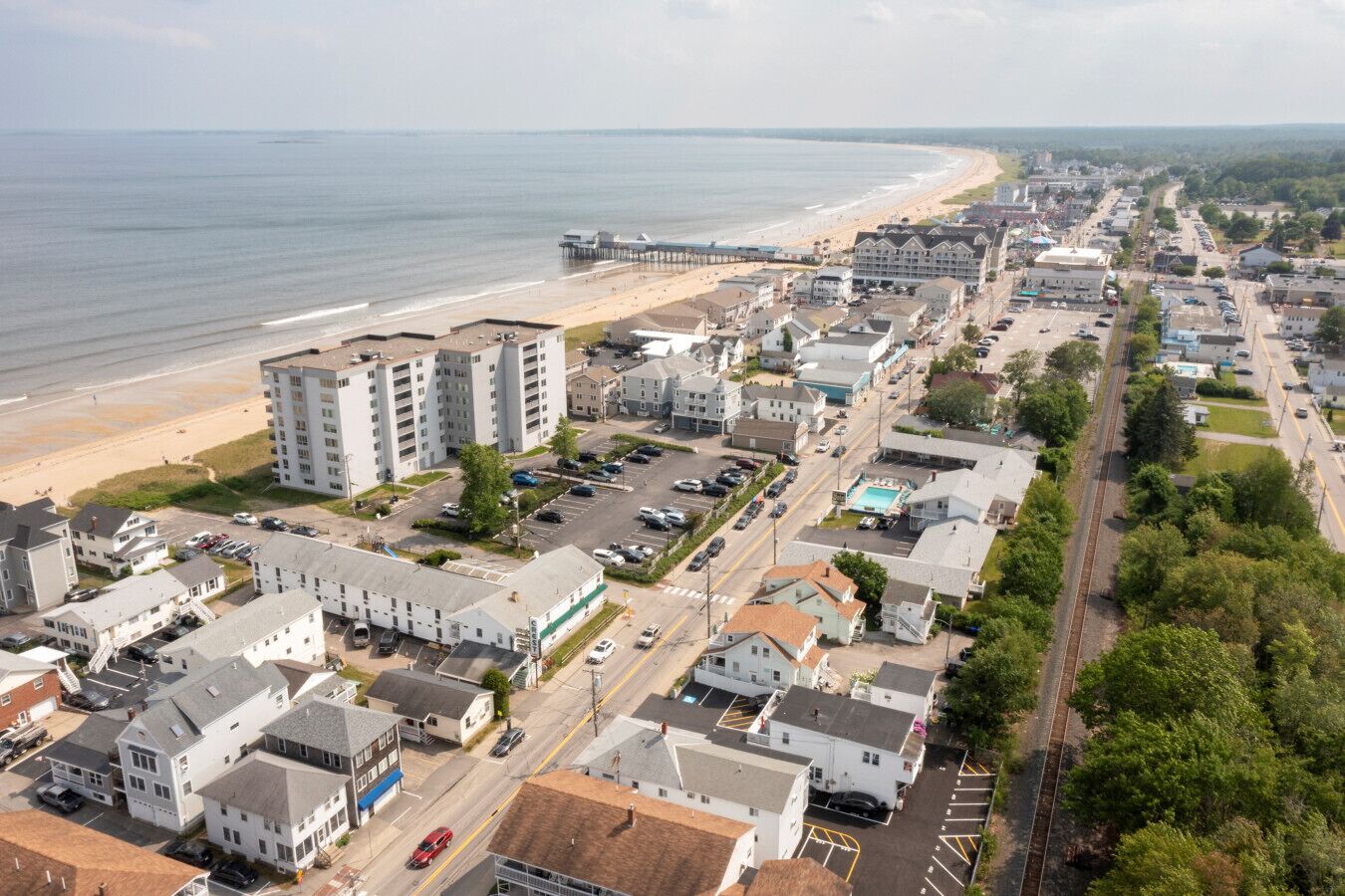 Un pueblo costero con playa, edificios de varios pisos y una línea de tren.