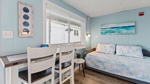 A room with a bed, a desk with chairs, a window, and a painting on the wall.