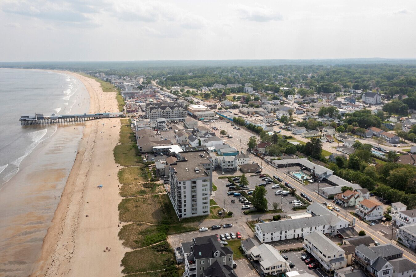An aerial view of a coastal town with a beach, a pier, and a mix of residential and commercial buildings.