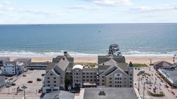 Een kusthotel met uitzicht op de oceaan, met een centraal gebouw met een koepel, meerdere vleugels, een parkeerplaats en een strandpromenade.