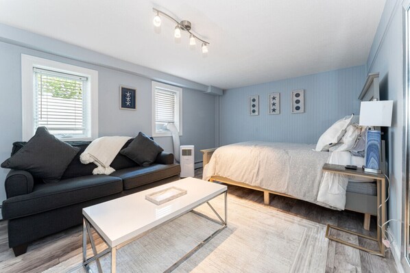 A modern bedroom with a bed, a sofa, a bedside table, and a window.