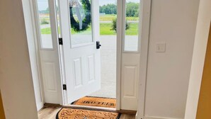 Un pasillo con piso de madera que conduce a una puerta con un felpudo que dice 'WELCOME'.