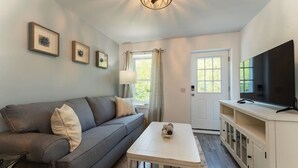 A living room with a grey sofa, a white coffee table, a TV on a cabinet, and framed pictures on the wall.