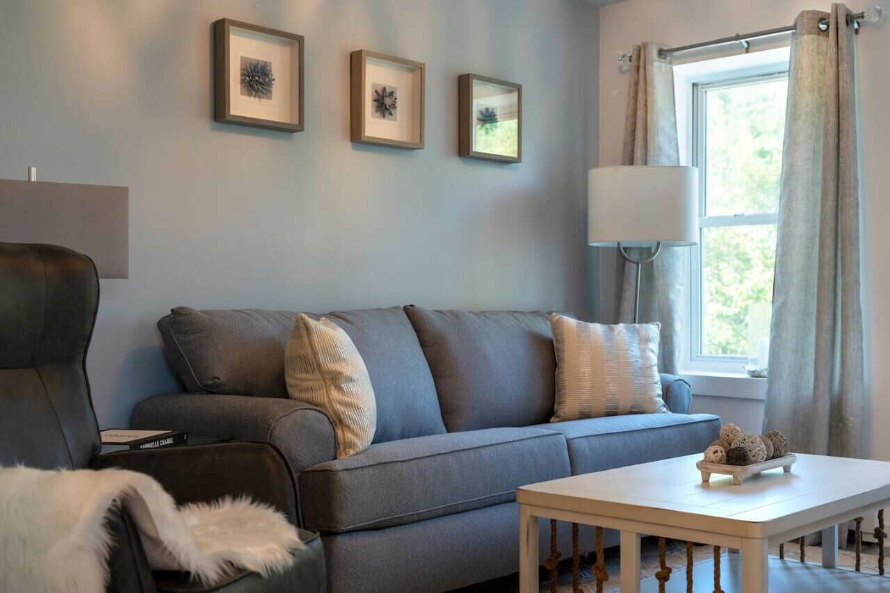 Una sala de estar con un sofá gris, una mesa de centro blanca y obras de arte enmarcadas en la pared.