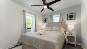A bedroom with a bed, a ceiling fan, a nightstand, and a window with curtains.