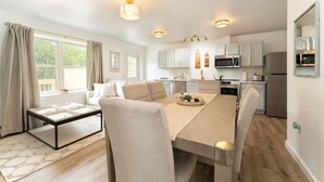 Una cocina moderna con armarios blancos, electrodomésticos de acero inoxidable y una zona de comedor con mesa y sillas.