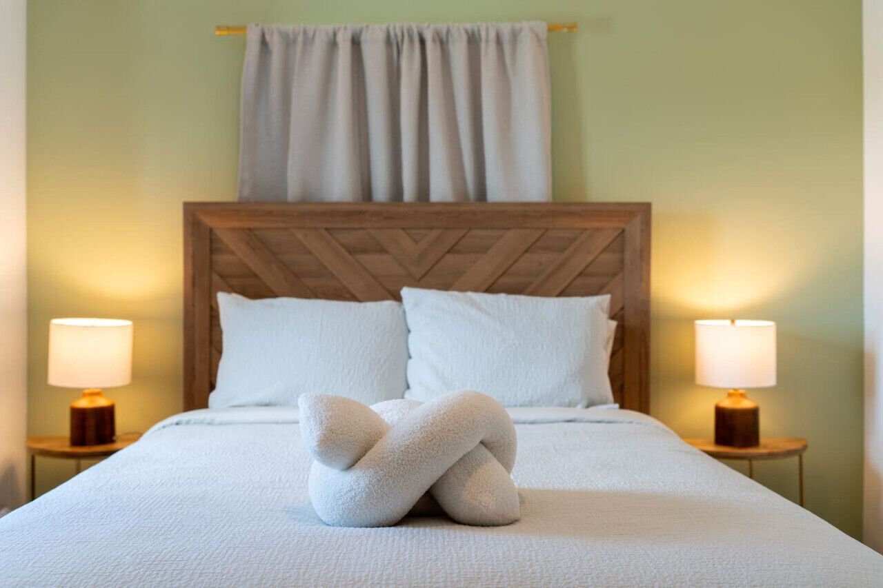 Una cama bien hecha con cabecera de madera, dos lámparas de noche y una toalla doblada sobre la cama.