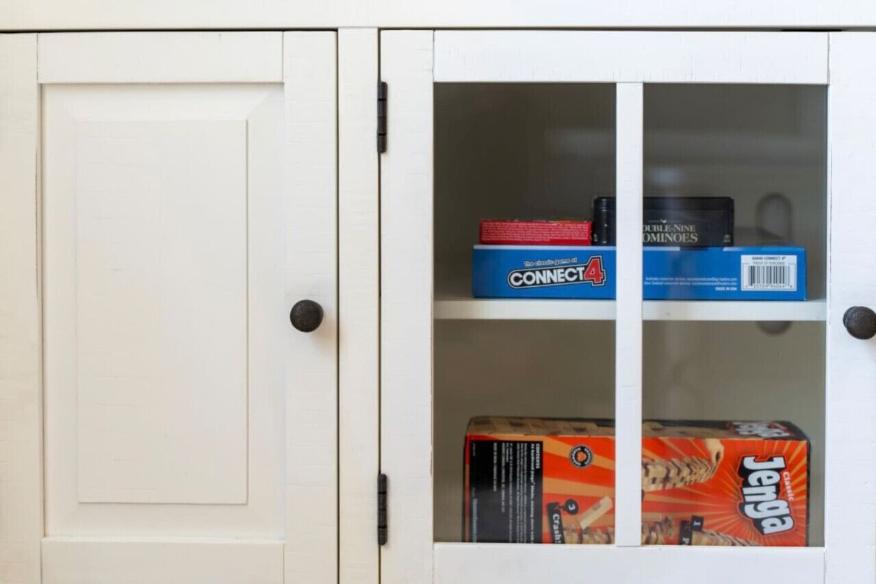 A white cabinet with glass doors containing Connect4, Dominoes, and Jenga boxes.