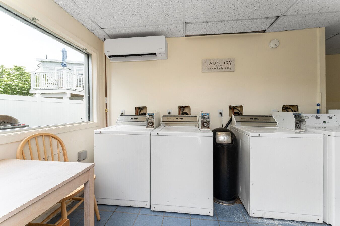 A laundry room with four washing machines, a table, and a chair.