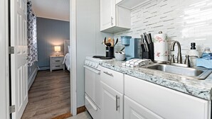 A modern kitchen with white cabinets, a marble countertop, and a built-in stove. There is a sink with modern faucets and a coffee maker on the counter. - Steps to Beach & Pier | First Floor Suite 462 (Old Orchard Beach)