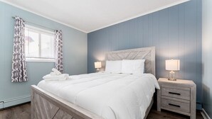 A neatly made bed with white linens, two bedside tables with lamps, and a window with patterned curtains. - Steps to Beach & Pier | First Floor Suite 462 (Old Orchard Beach)