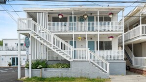 A two-story building with a white exterior, a central staircase, and multiple balconies with hanging flower baskets. - Cozy 1 BR Suite Steps to the Beach (469) (Old Orchard Beach)