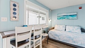 A room with a bed, a desk, and chairs. There is a window with blinds, a painting on the wall, and a small table with a plant. - Beachside Getaway | Walk to Pier & Downtown (463) (Old Orchard Beach)