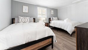 A hotel room with two beds, each with white bedding and a wooden headboard. There are two bedside tables with lamps, and the walls are painted light grey.