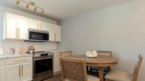 A modern kitchen with white cabinets, a microwave, stove, and a dining table with chairs.
