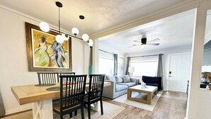 A spacious living room with a wooden dining table, black chairs, a grey sofa, and a coffee table. There is a ceiling fan and a painting on the wall. - 2br-newly Renovated Full Kitchen-3 Mins Asia Dist (Oklahoma City)