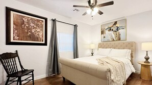 A bedroom with a bed, two bedside tables with lamps, a ceiling fan, a window with curtains, a chair, and two wall-mounted paintings. - 2br-newly Renovated Full Kitchen-3 Mins Asia Dist (Oklahoma City)