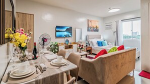 Een moderne hotelkamer met een zithoek, een bed met kleurrijke kussens, een groot raam en kunstwerken aan de muren.