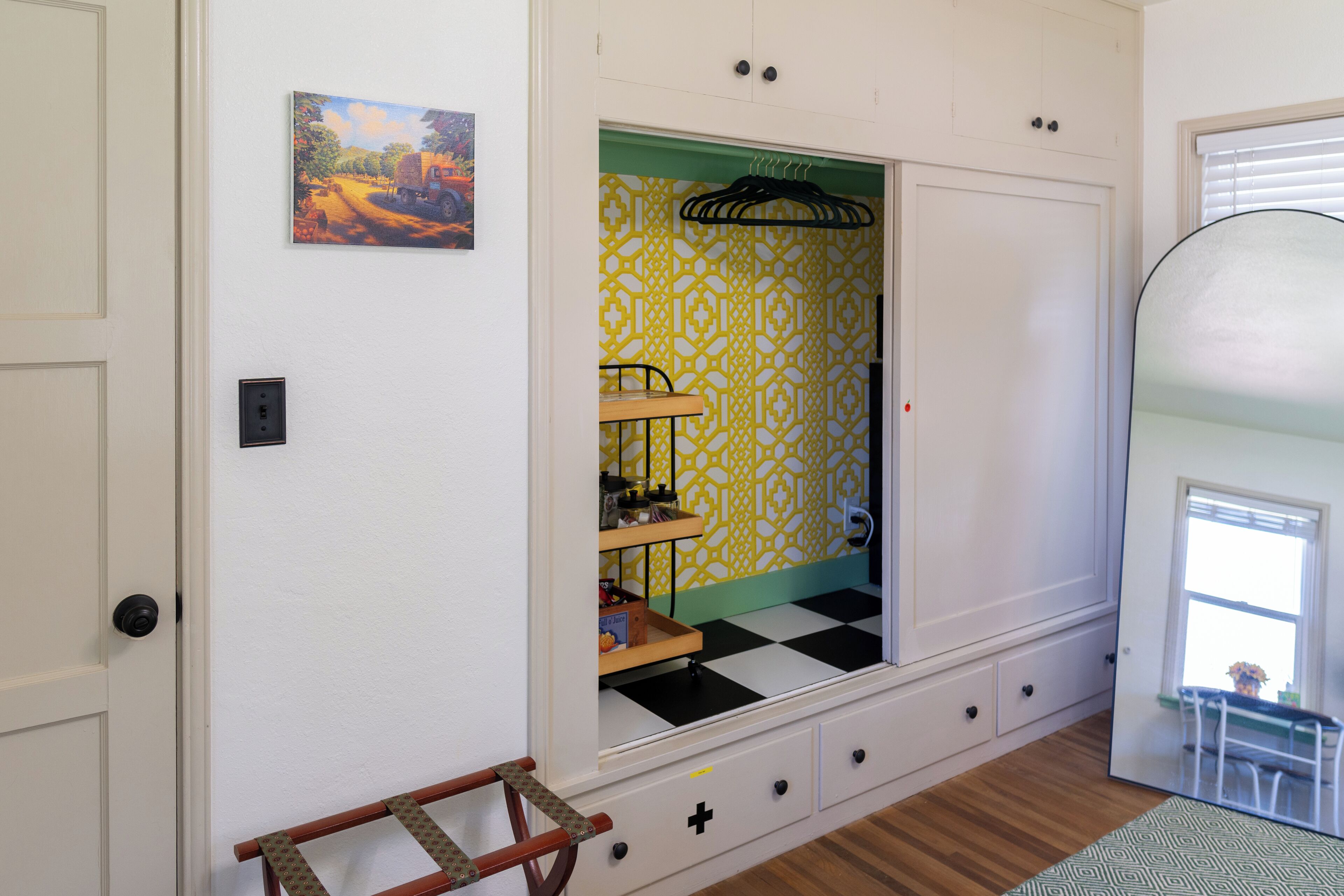 A room with a checkered floor, a mirrored wardrobe, a patterned wall, and a small table with a chair.