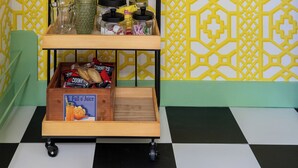 Une pièce avec un sol à carreaux, un chariot en bois contenant divers objets et un mur jaune à motifs.