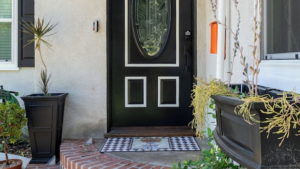 Une entrée de maison avec une porte noire, une marche en briques et des plantes en pot.