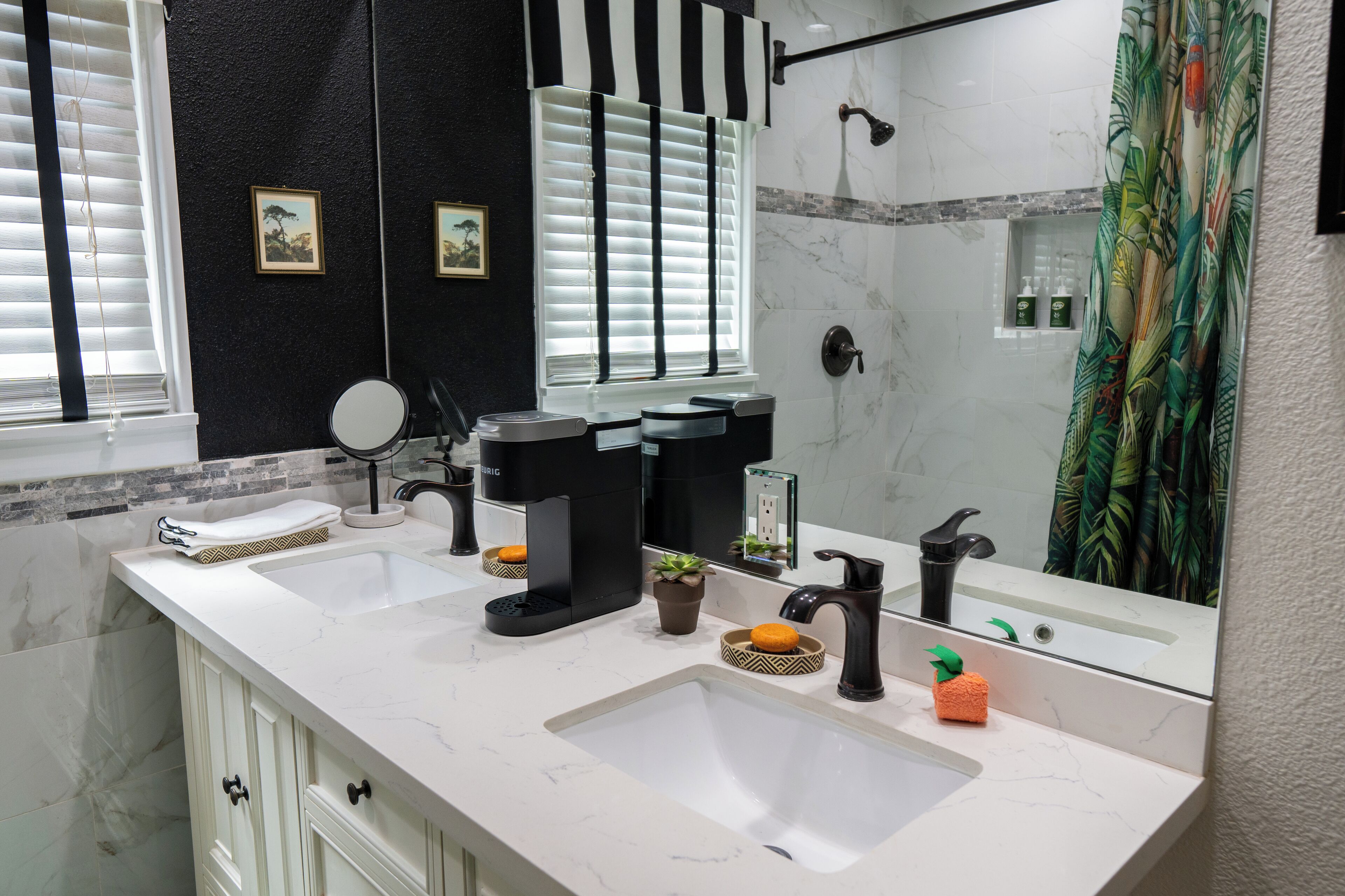 Un baño con dos lavamanos, un espejo, ducha y ventana con persianas.
