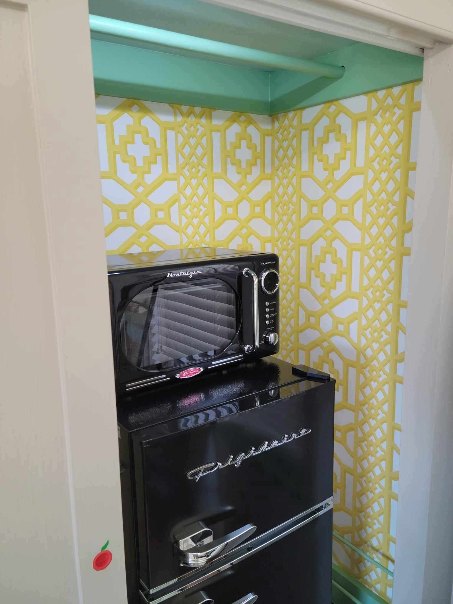 Ein kompakter Kühlschrank mit integriertem Mikrowellenherd, in einer kleinen Küche mit einer Wand in gelb-weißem Muster.