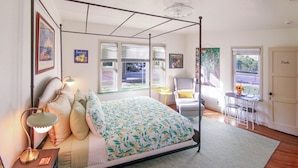 Un lit à baldaquin avec une couvre-lit à motifs floraux, une table de chevet avec une lampe et une chaise avec un coussin jaune.