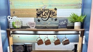 Una estación de café con una cafetera Keurig, una jarra de café y un colgador para tazas.