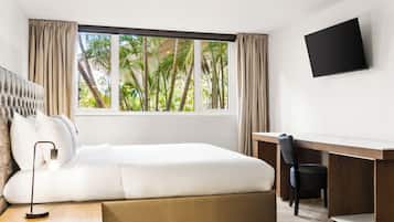 A modern hotel room with a large bed, a desk, and a TV on the wall.