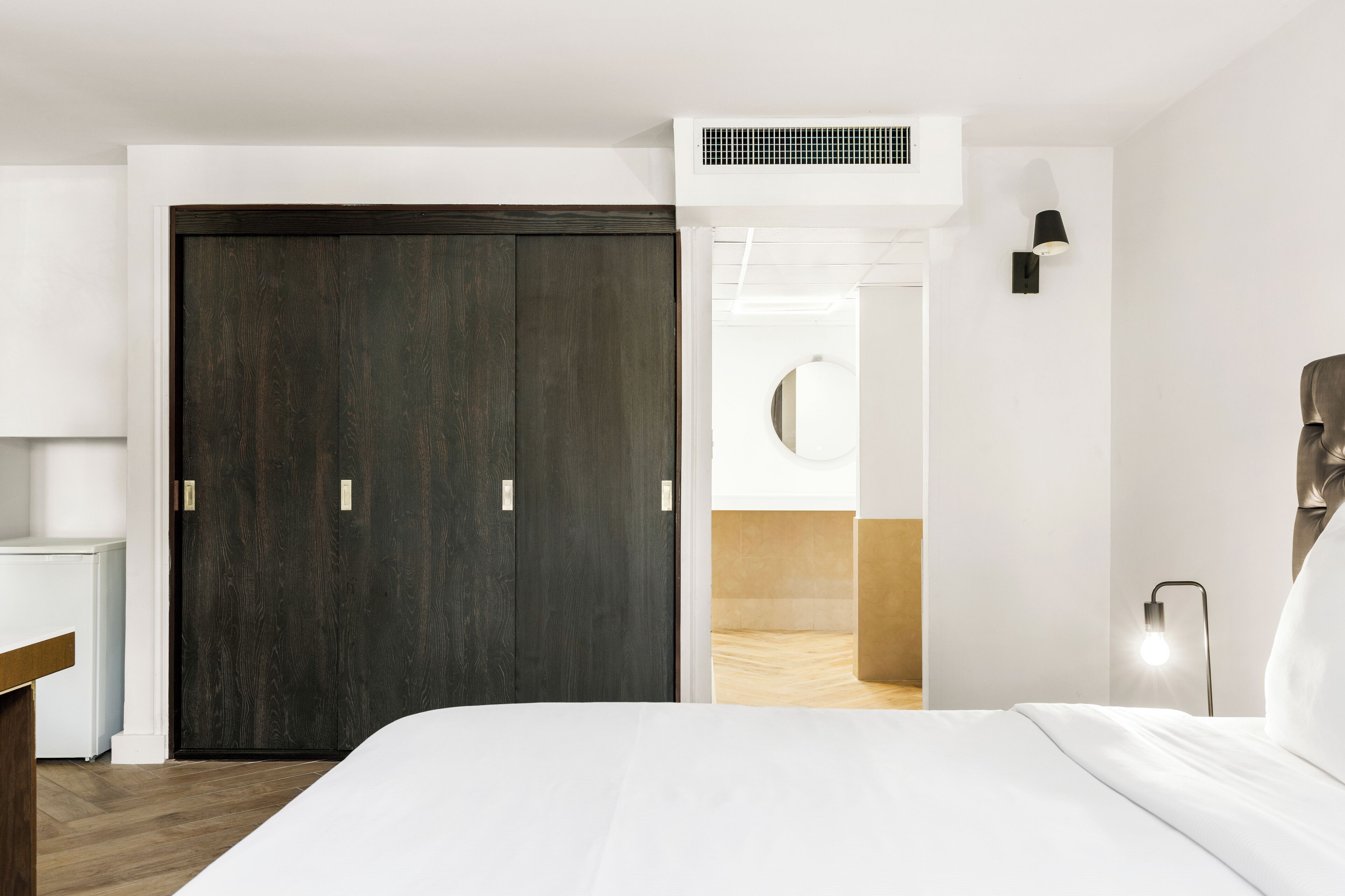 Ein modernes Schlafzimmer mit einem dunklen Holzschrank, einem weißen Bett und einer Nachttischlampe.