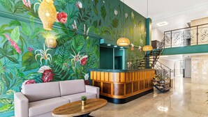 A lobby with a sofa, a wooden reception desk, a staircase, and a mural of tropical foliage. - Parasasa Hotel Curacao (Willemstad)