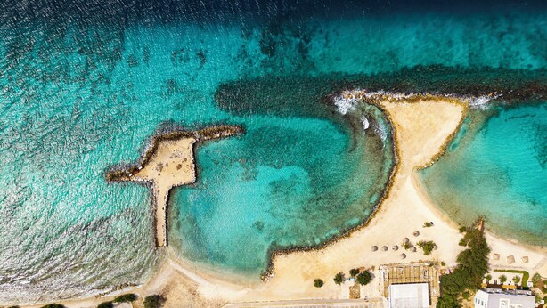 An aerial view of a coastal area with a sandy beach, a parking lot, and a building with a flat roof. - Parasasa Hotel Curacao (Willemstad)