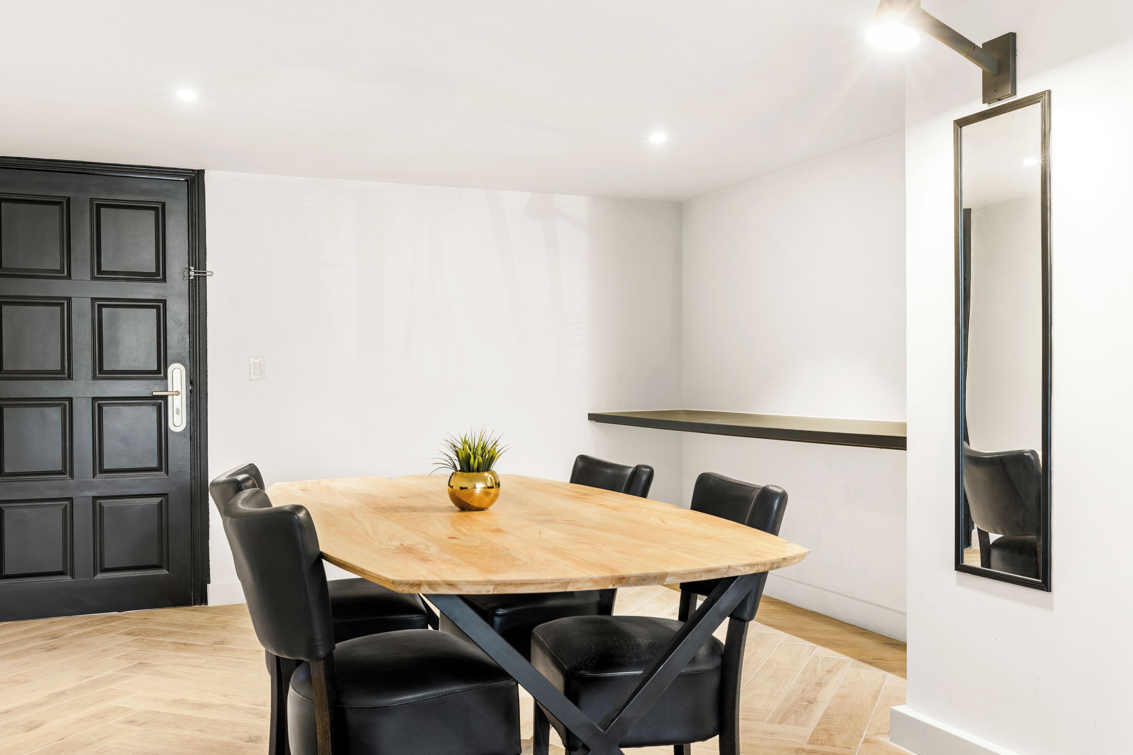 A conference room with a wooden table, black chairs, a potted plant, and a black door.