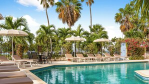 A pool area with lounge chairs and umbrellas, surrounded by palm trees and a clear sky. - Parasasa Hotel Curacao (Willemstad)