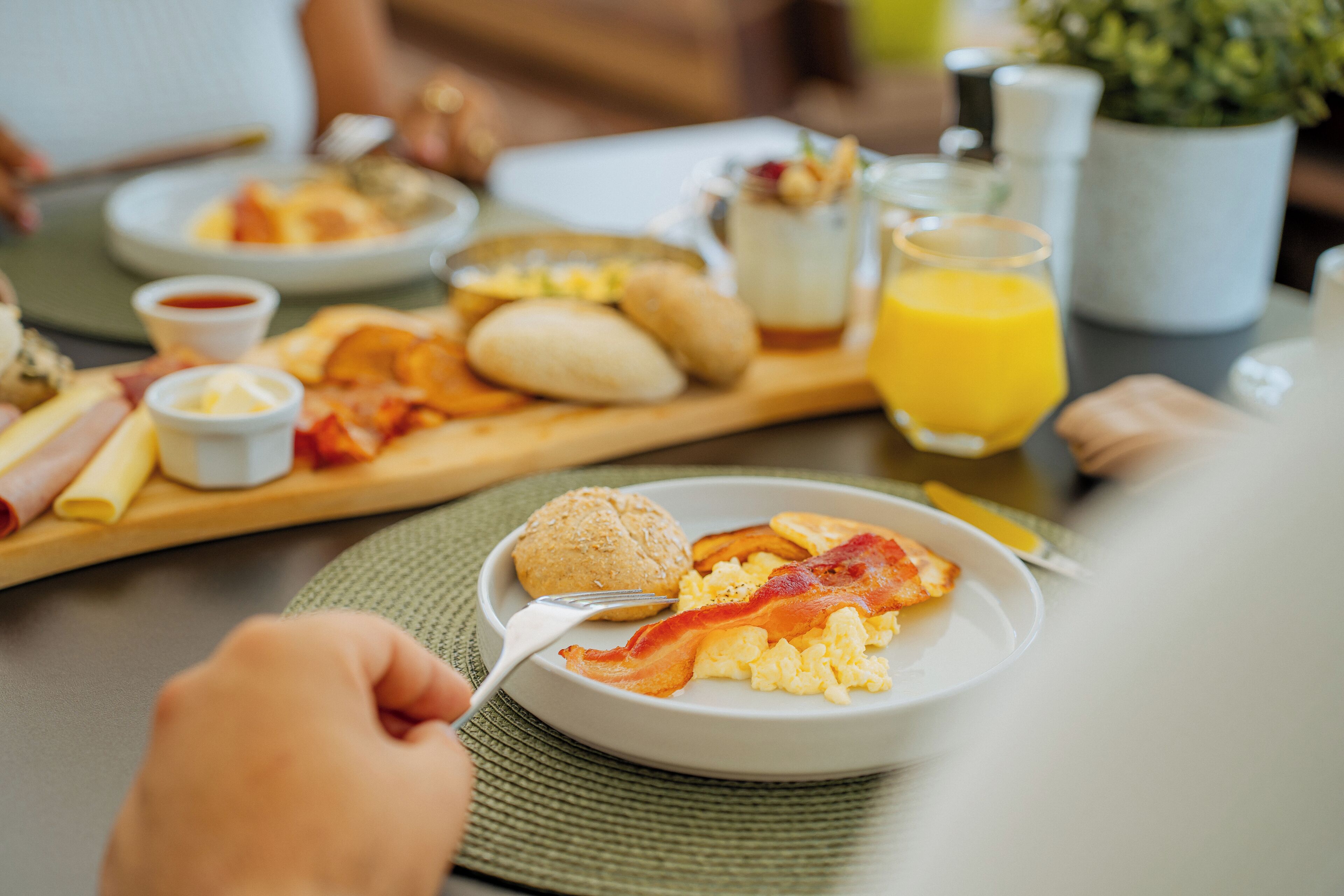 A breakfast setting with a plate of scrambled eggs, bacon, and toast, accompanied by a glass of orange juice and a cup of coffee.