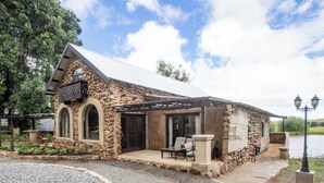 A stone building with a covered porch and outdoor seating area. - Lake Villa Room 15 (Swartberg)