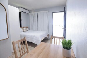 Een slaapkamer met een bed, een houten tafel, een kamerplant en een schuifdeur naar een balkon.
