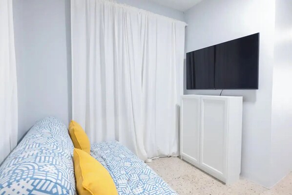 Een slaapkamer met een bed, witte gordijnen, een wandtelevisie en een radiator.