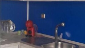 A compact kitchen with light wooden cabinets, a washing machine, a red coffee maker, and a blue backsplash. - Apartment in fair area (Albacete)