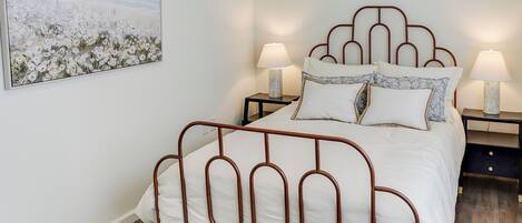 A neatly made bed with a metal frame, two bedside tables with lamps, and a large painting on the wall.