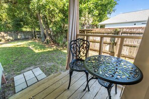 A wooden deck with a metal table and chairs, surrounded by a wooden fence and trees.