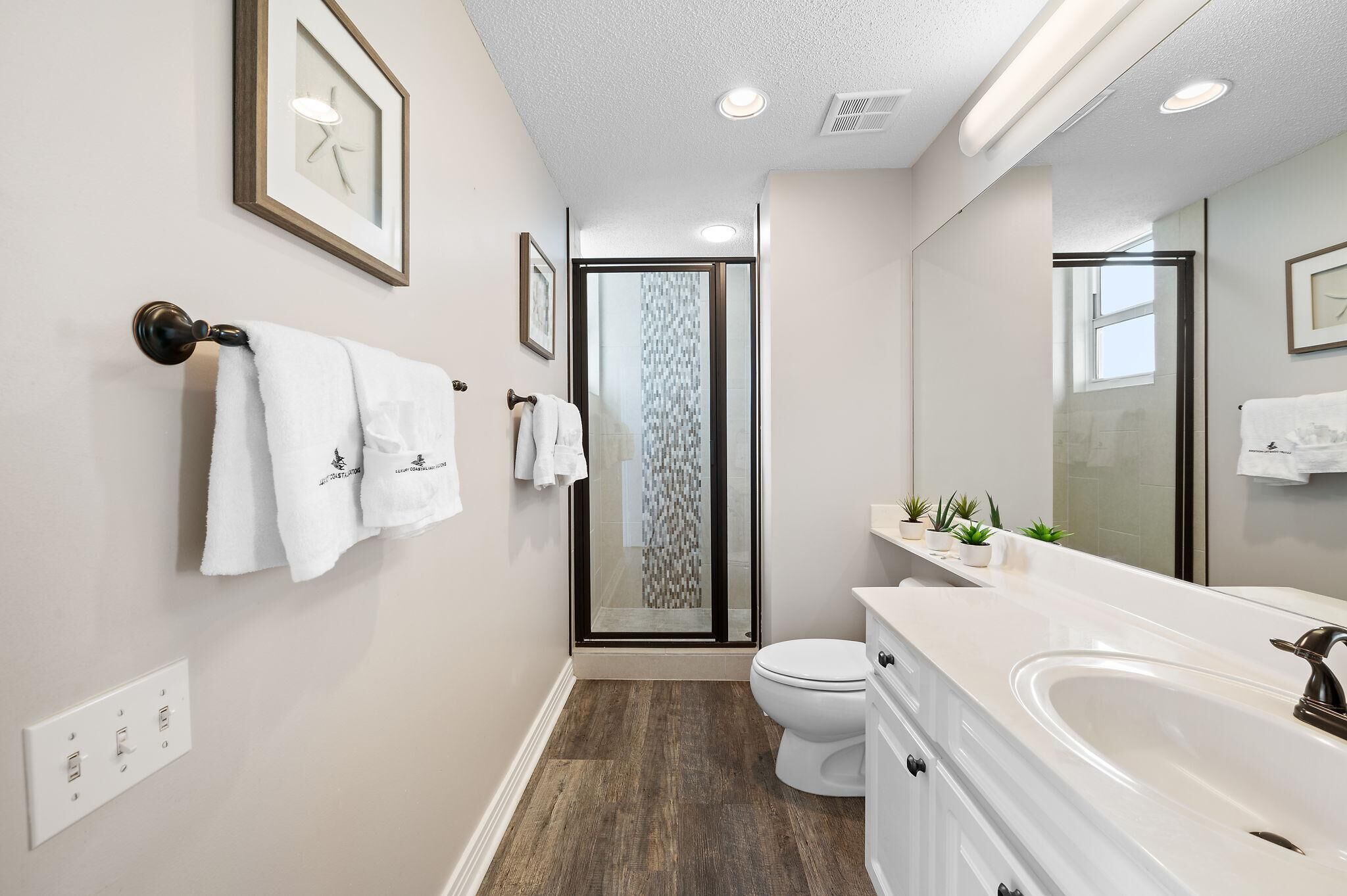 A modern bathroom with a large mirror, a glass shower enclosure, a white toilet, and a vanity with a sink.