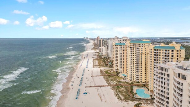 Un hôtel situé sur la côte, avec vue sur la plage, de nombreux balcons et une piscine.