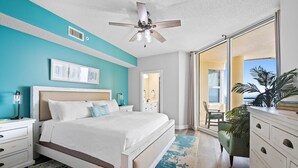 Une chambre à coucher comprenant un lit, des tables de chevet, une commode, un ventilateur de plafond et une vue sur l’extérieur.