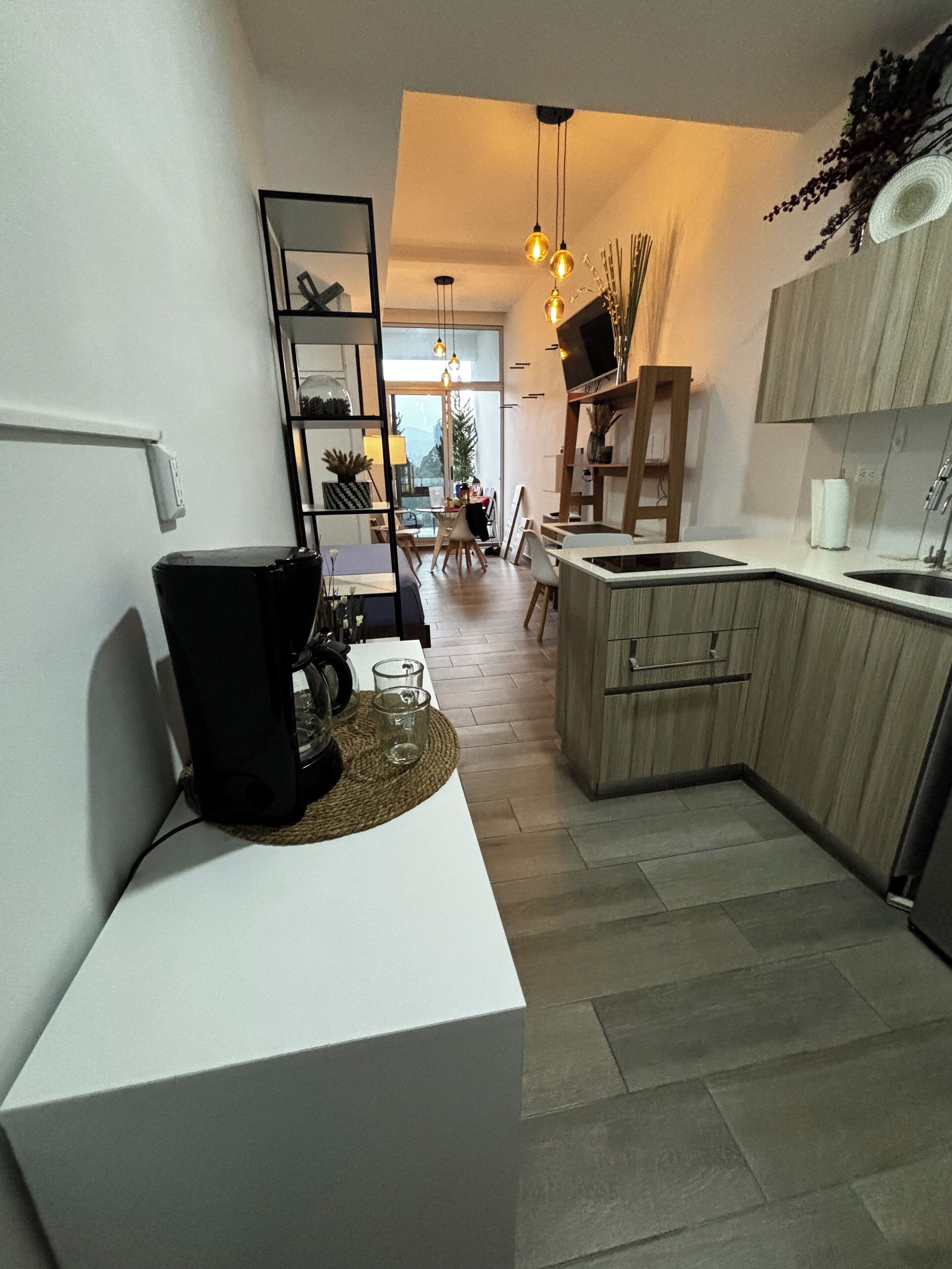 A modern kitchen with a white countertop, wooden cabinets, and a built-in island. There is a dining area with a table and chairs, and a large window providing natural light.