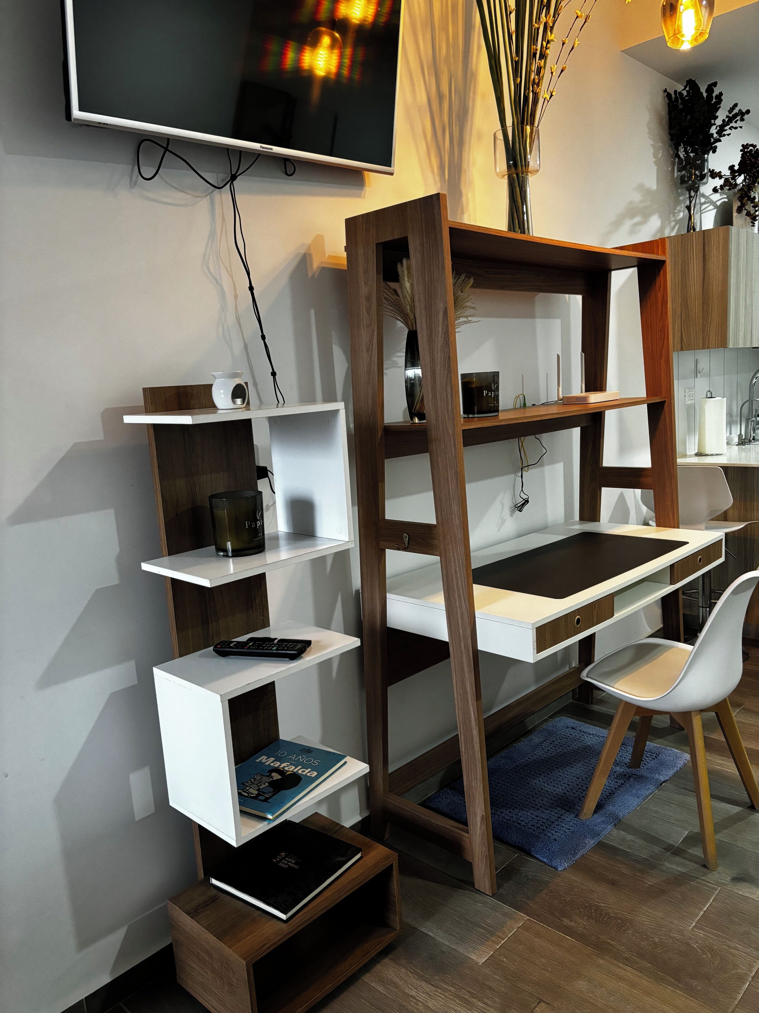 Una oficina en casa moderna con un escritorio de madera, estanterías blancas, una silla blanca y un televisor montado en la pared.