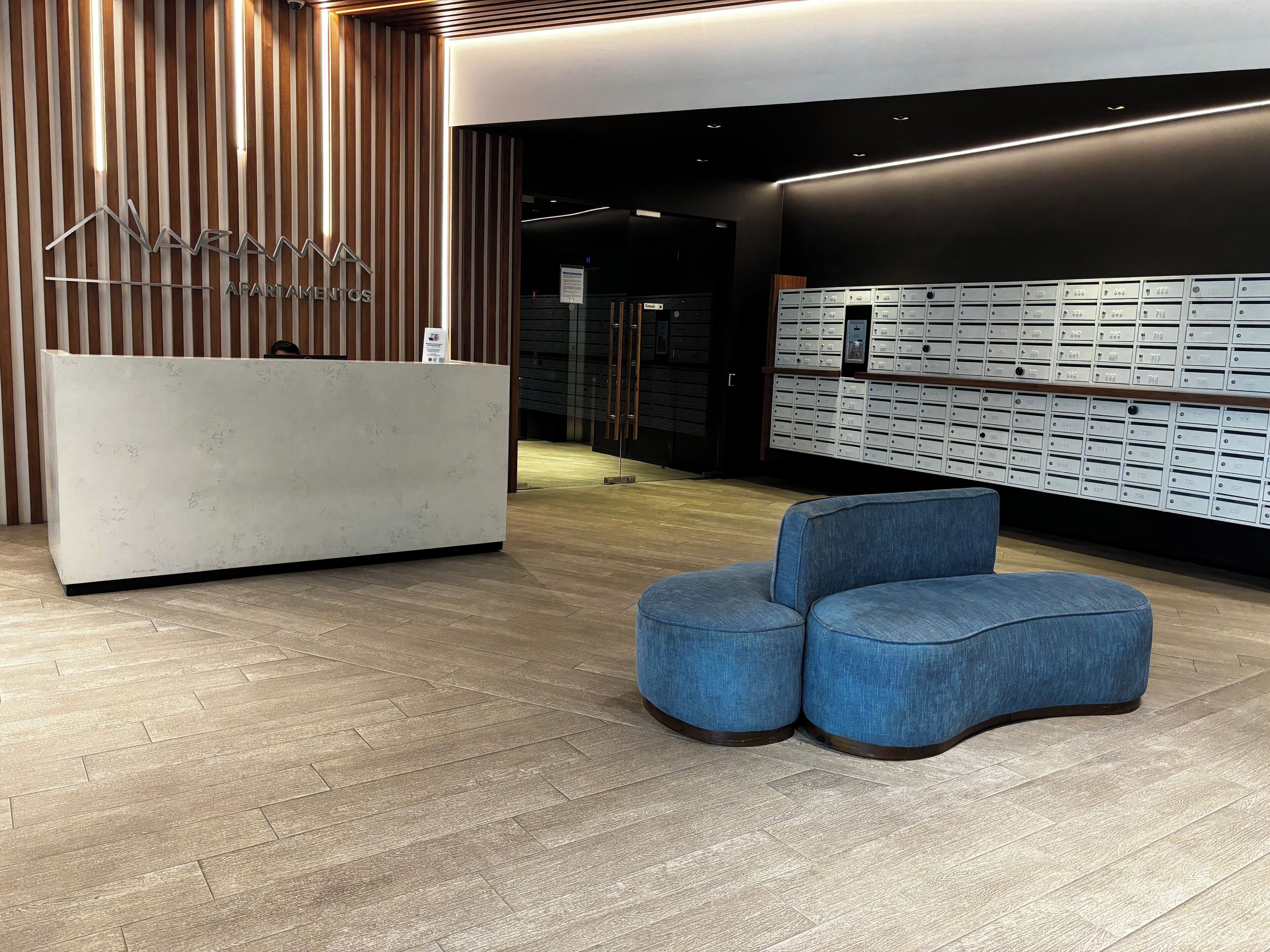 Un espace d’accueil au design moderne, comprenant un comptoir de réception, un ensemble de boîtes aux lettres et un coin salon.
