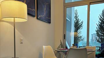Una habitación moderna con una mesa de vidrio, sillas blancas, una lámpara de pie y una obra de arte en la pared.