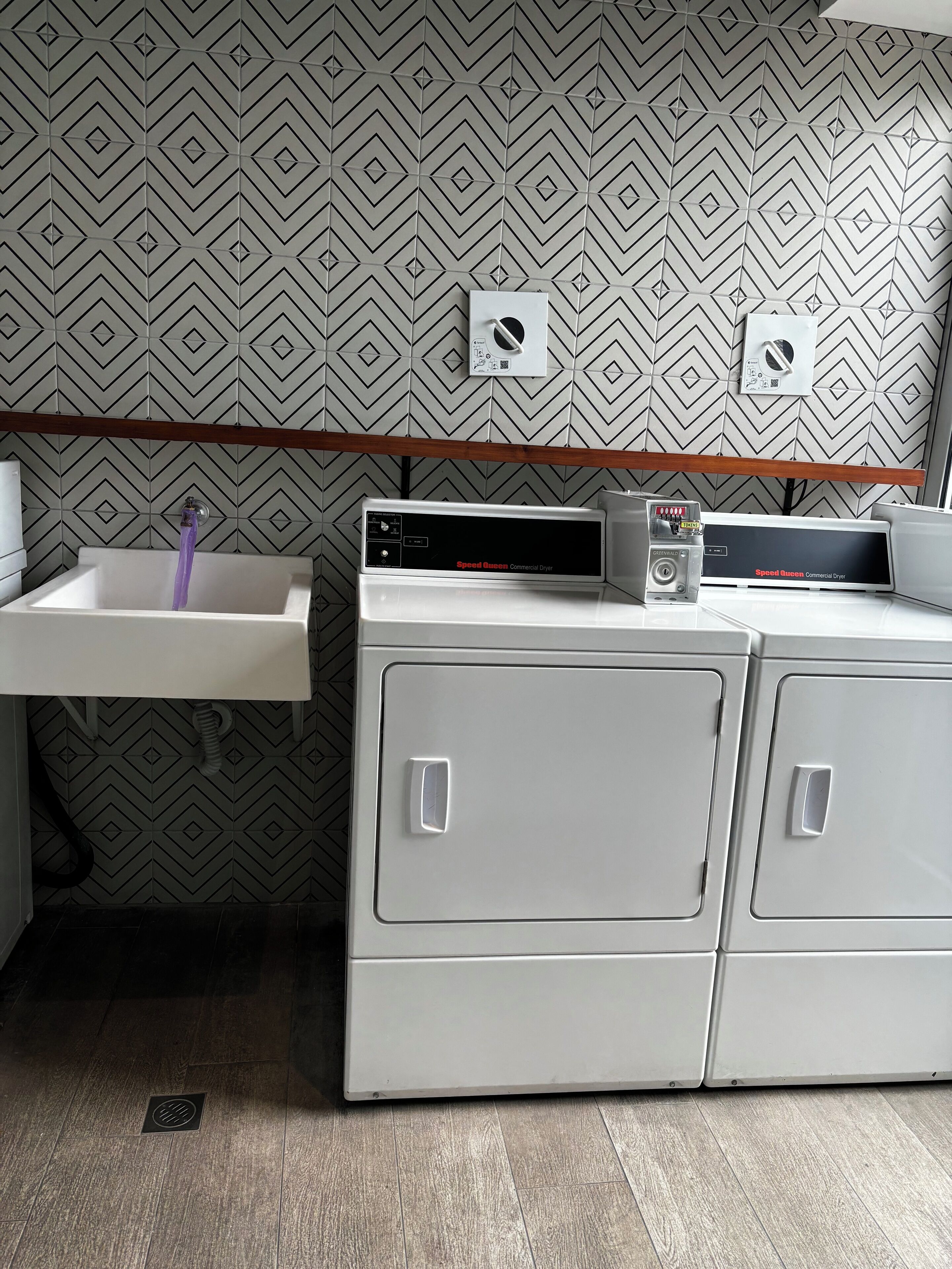 A laundry area with a sink, two dryers, and a patterned wall.